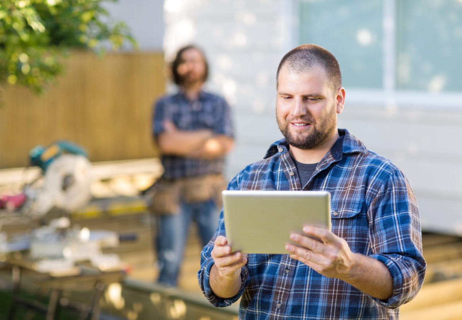 Carpenter Using Digital Tablet With Coworker Standing In Backgro
