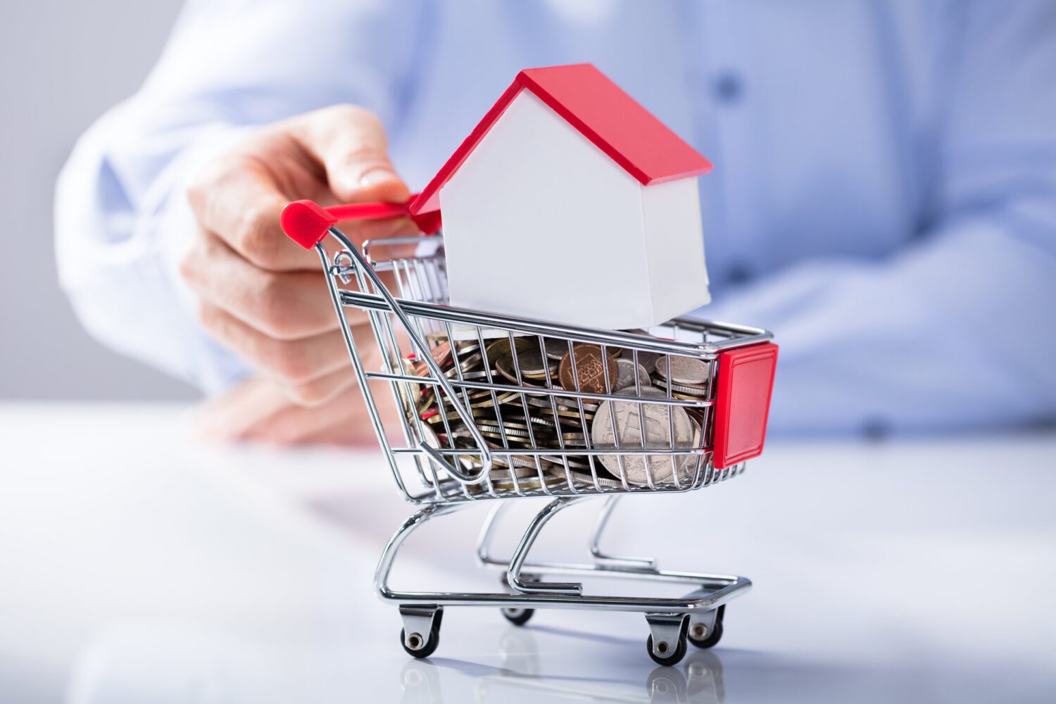 Man Holding Shopping Cart Filled With Coins And House Model